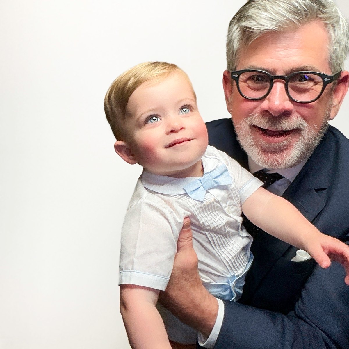 Grandfather in a navy suit holding a smiling toddler in a bow tie at a Galveston wedding photo booth